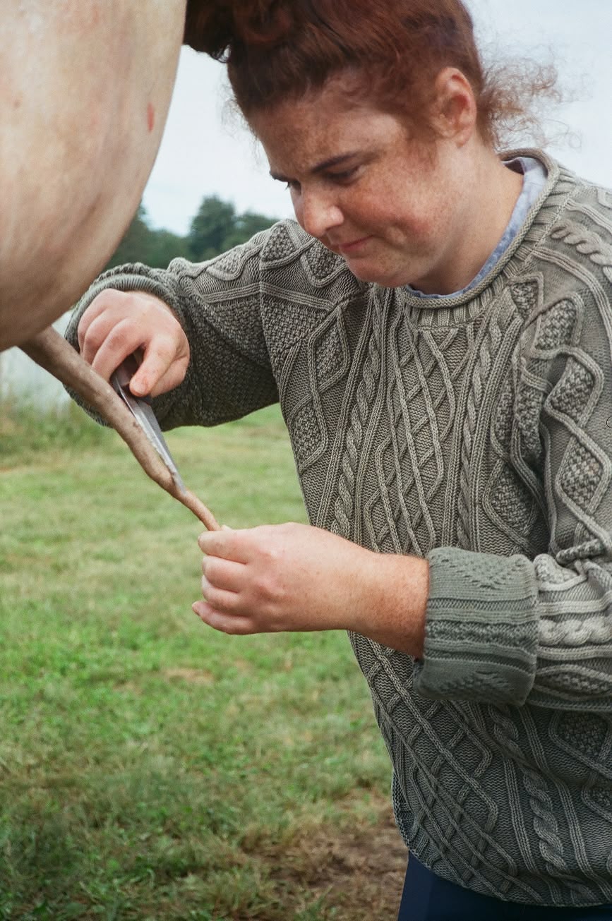 A woman in a cable-knit sweater tending to livestock in a field.