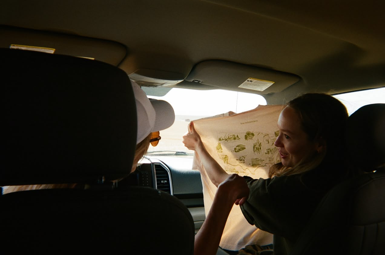 Two people in a truck cab holding up a screen-printed t-shirt against the light.